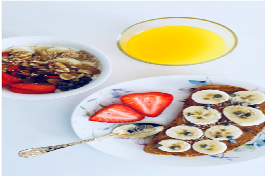 A bowl of yogurt and fruit with granola, toast with banana slices, and a glass of juice.