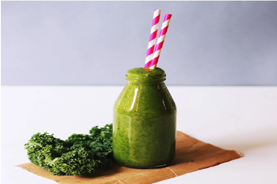 A green kale smoothie in a bottle with two straws inside.